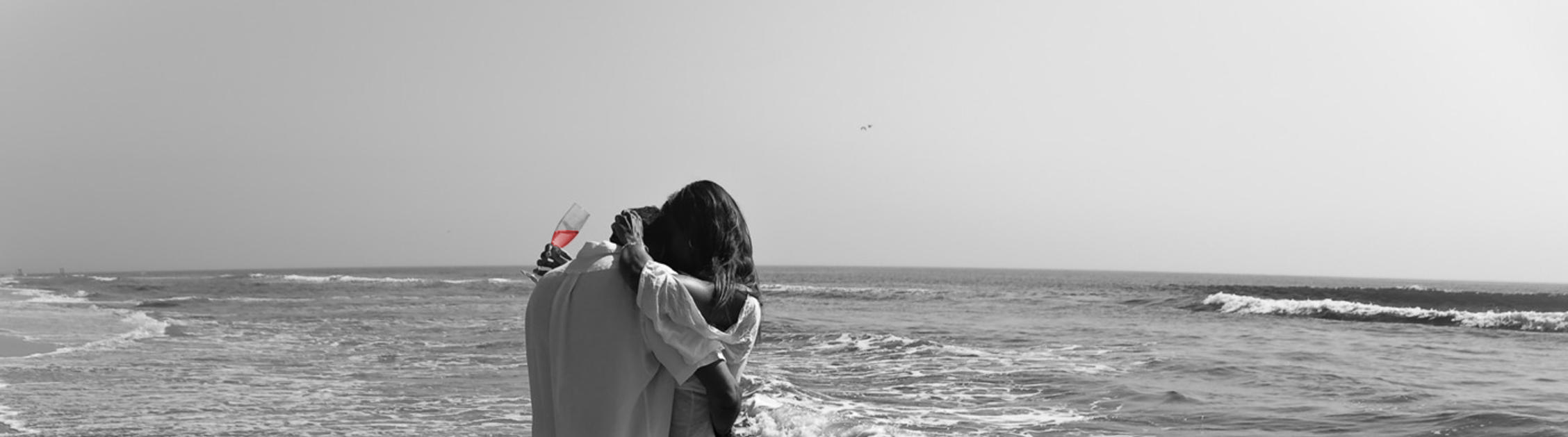 a couple hugging romantically on the beach, the woman is holding a champagne flute